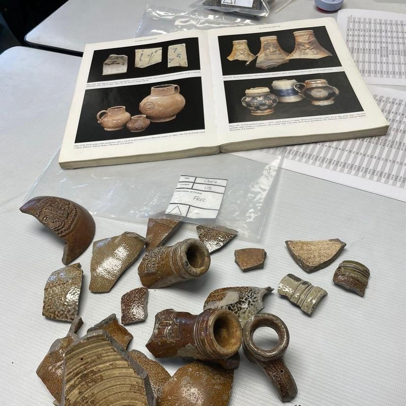 Fragments of bartmann jug on a table< behind is a book with images of bartmanns