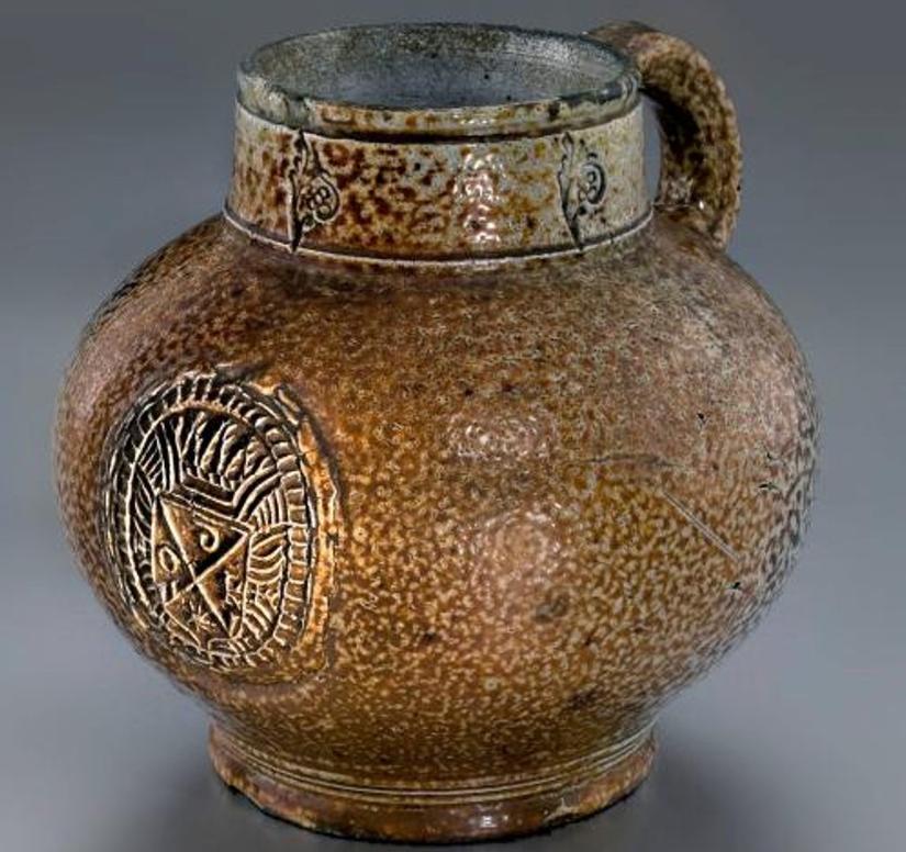 A bartmann jug with a metal lid. The medallion on the front of the mug has the letters IODK in it.