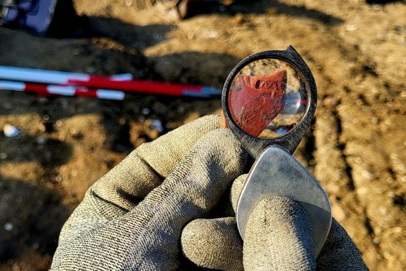 Piece of samian ware Roman pottery seen through a magnifying glass during excavations