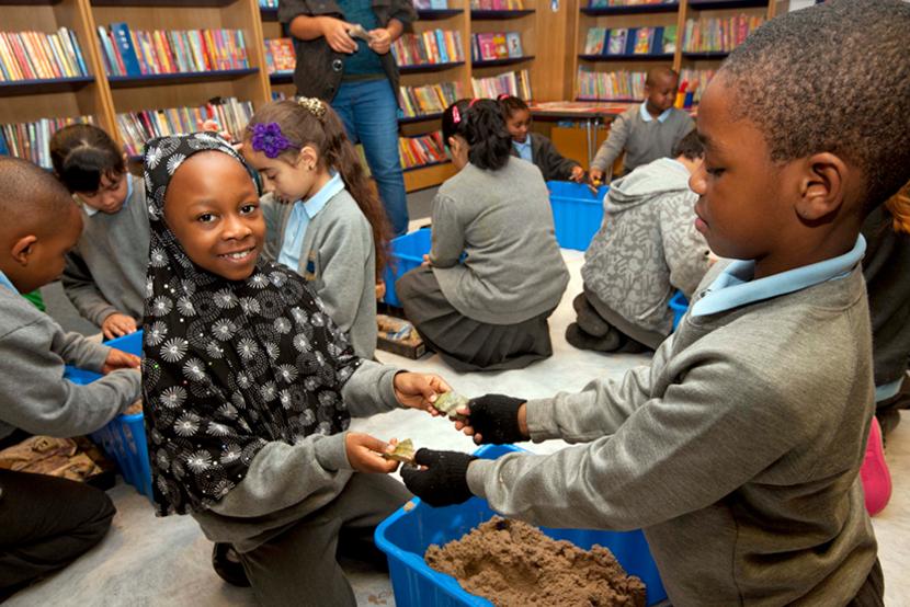Two schoolchildren discover artefacts within a 'digbox' - a sandpit containing various buried objects.