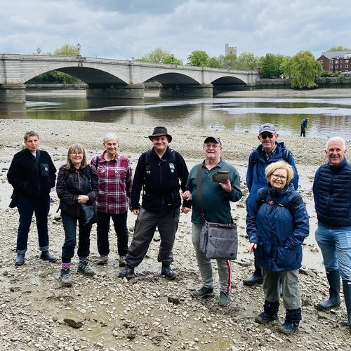 A group of walk attendees stand smiling with their backs to the river and Putney Bridge