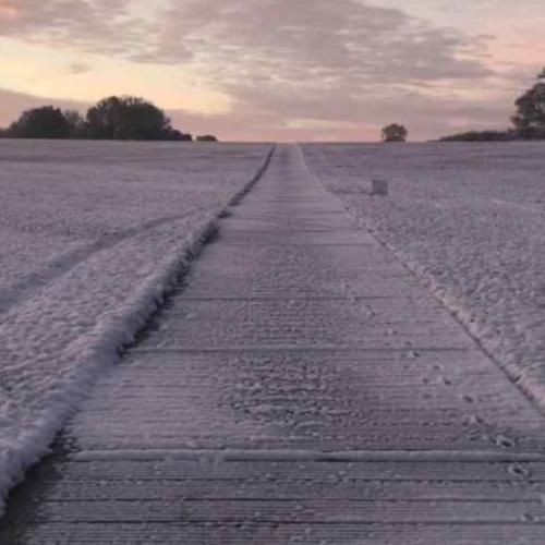 Temporary metal trackway running uphill through a field. The trackway and field are covered in snow