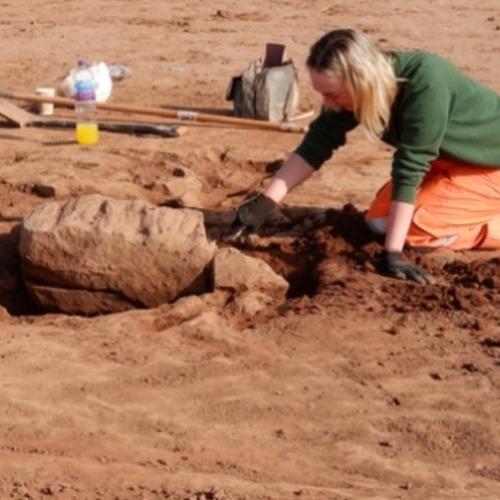 Archaeologist excavating a large masonry stone