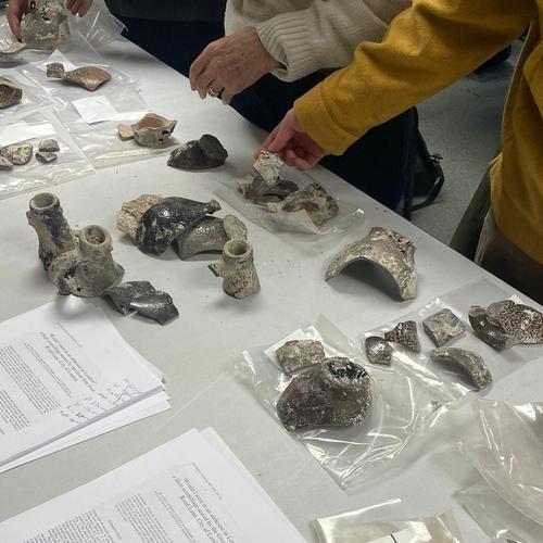 Pottery laid out on a table with hands reaching for it